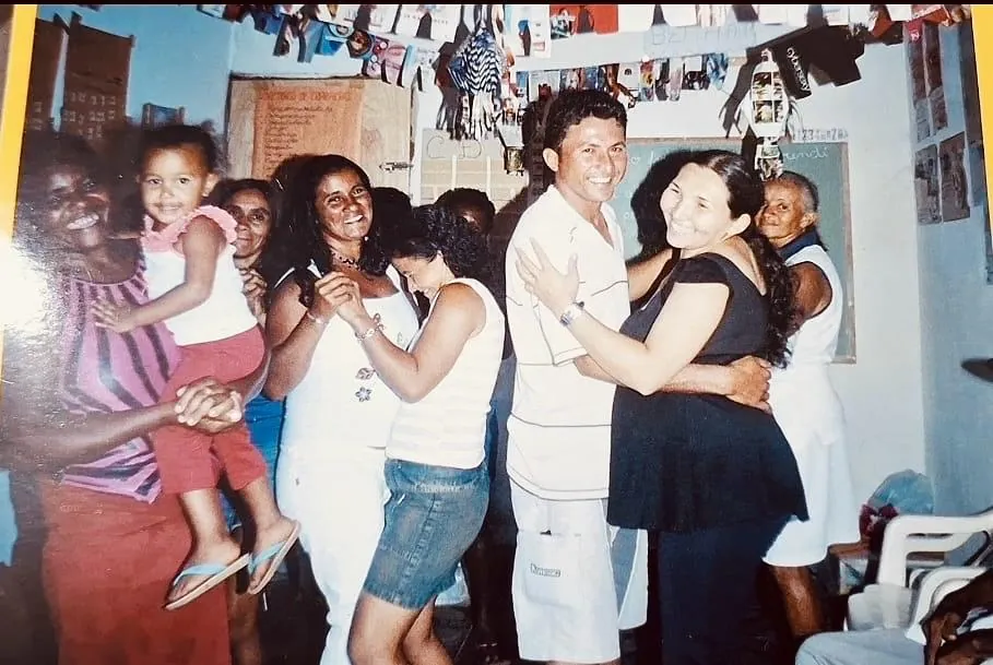 Foto antiga do pai e da mãe de Lanna dançando na garagem de casa, cercados pelos alunos de EJA.