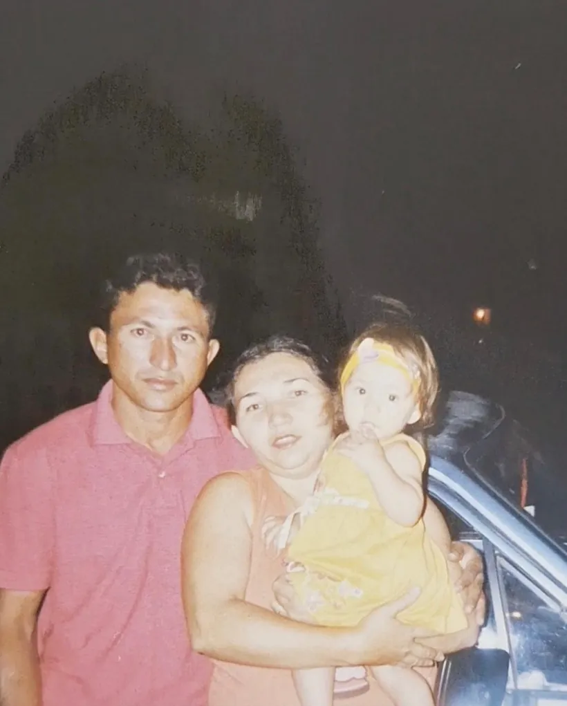 Foto antiga do pai e da mãe de Lanna, com ela ainda bebê no colo da mãe.