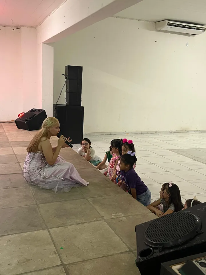 Lanna Campos fantasiada, sentada em um salão, cercada de crianças em uma festa.
