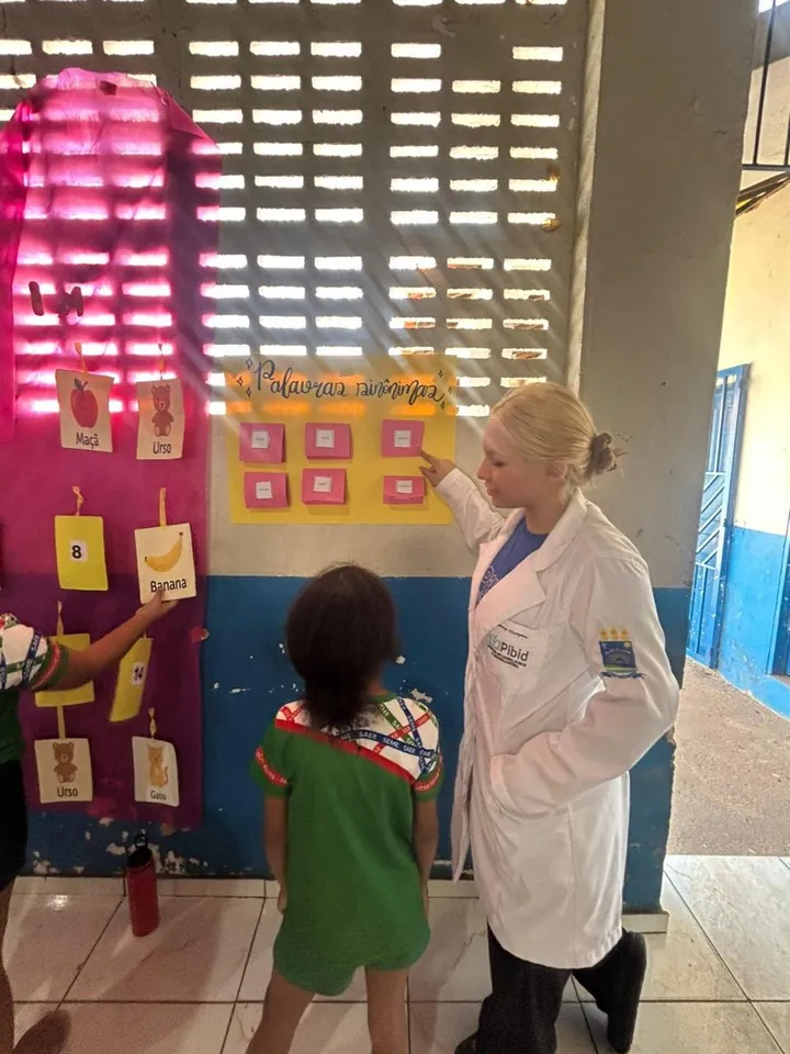 Lanna Campos de jaleco ao lado de uma criança diante de um painel colorido na escola.