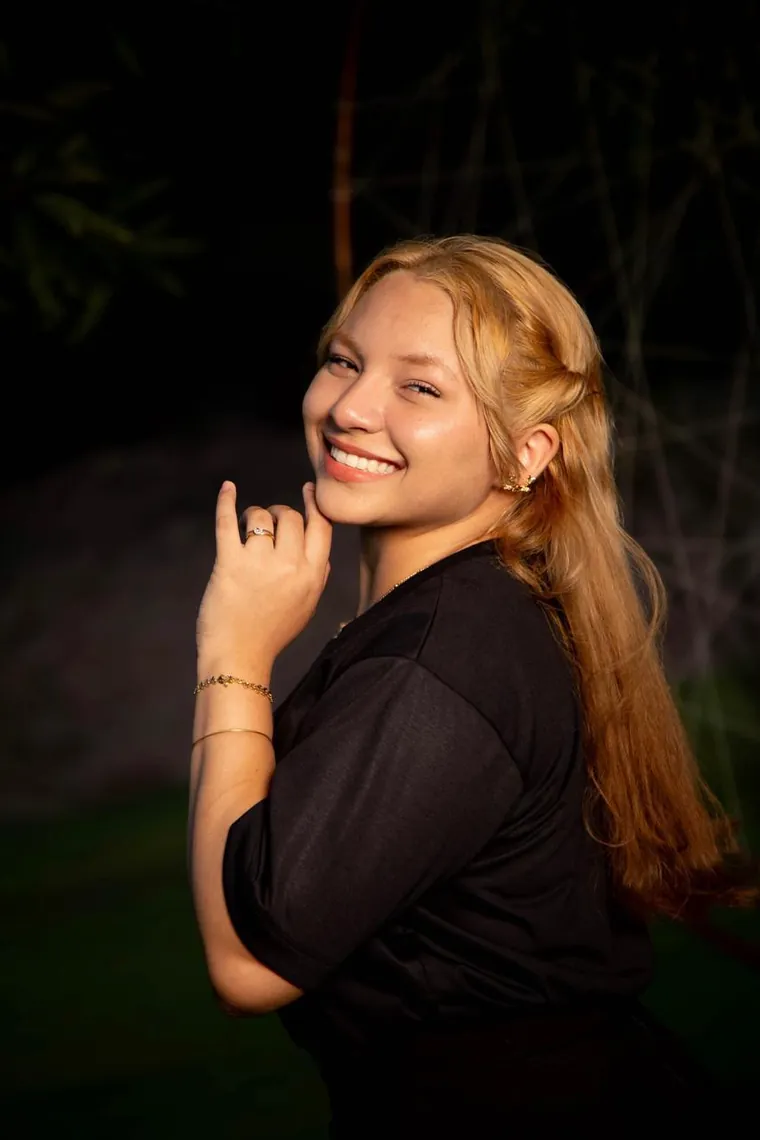 Lanna Campos sorrindo, com a mão junto ao rosto, ao entardecer.